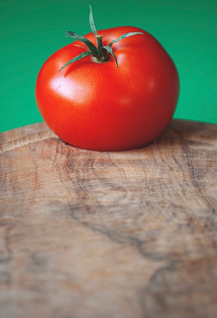 Pomodoro rosso su un tagliere di legno su sfondo verde. Preso da una fotocamera da vicino.