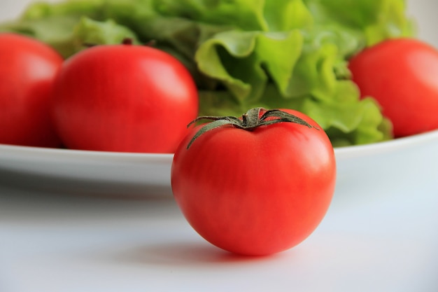 Pomodoro rosso succoso di fronte a un piatto con insalata verde e pomodori