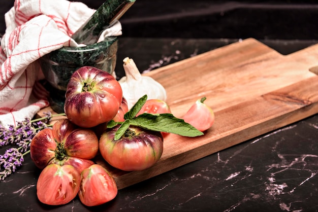 Pomodoro tigre su un tagliere con foglie di basilico su fondo in legno Pomodoro fresco wased per cucinare Pomodoro con goccioline d'acqua