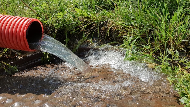 Pompaggio di acqua dalla zona alluvionale. Sistema fognario. Acque reflue industriali. Scarichi fognari da un tubo di fognatura rosso ondulato in plastica in un tombino fognario in città.