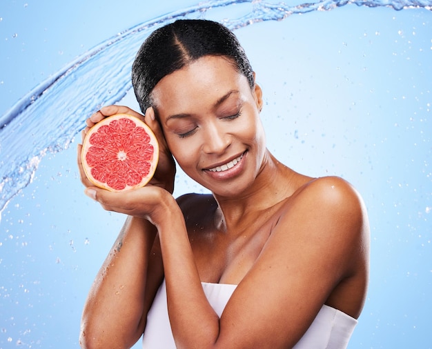 Pompelmo nero donna e spruzzi d'acqua bellezza e cura della pelle vitamina c e cosmetici naturali sani di benessere del corpo su sfondo blu studio Felice modello africano agrumi bagnati e nutrizione