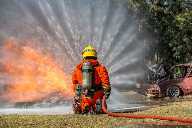 Pompiere che usando estintore e acqua dal tubo per la lotta antincendio