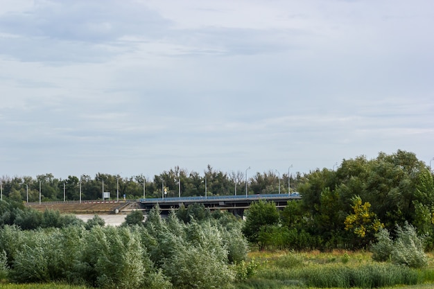 Ponte stradale che passa attraverso un campo con alberi e cespugli. Panorama.