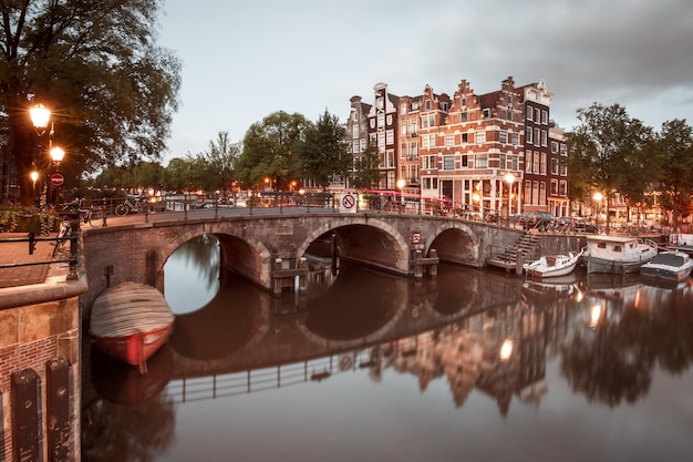 Ponte sul canale di Amsterdam e case tipiche barche e biciclette durante l'ora blu del crepuscolo serale holla...