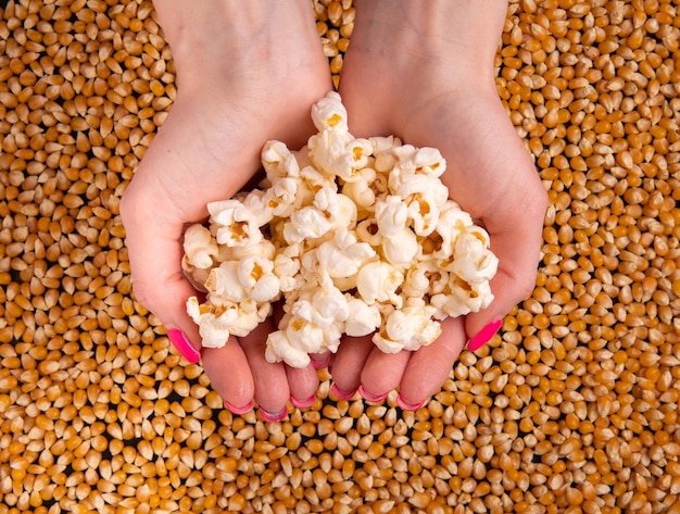 Popcorn al caramello nelle mani vista dall'alto sullo sfondo dei chicchi di mais