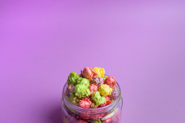Popcorn aromatizzato alla frutta multicolore in tazze di vetro su fondo rosa. Popcorn ricoperto di caramelle.