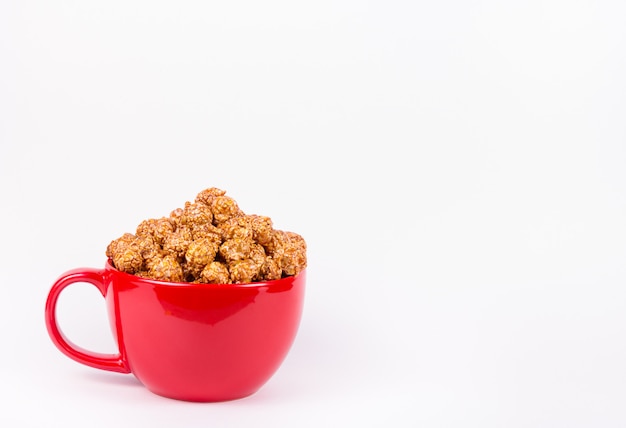 Popcorn caramellato dorato in ciotola rossa su fondo bianco