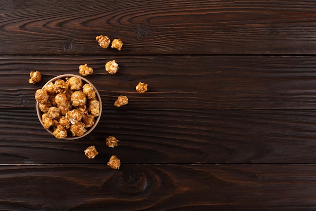 Popcorn caramellato nel secchio di carta sul tavolo da cucina in legno piatto