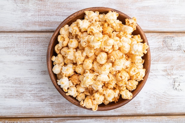 Popcorn con caramello in ciotola di legno su un fondo di legno bianco. Vista dall'alto, piatto laico, da vicino.