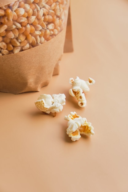 Popcorn cotto in una ciotola di vetro e chicchi di mais in una scatola di carta su una superficie beige beige