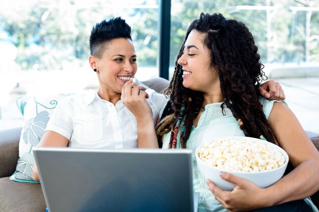Popcorn d'alimentazione della donna al suo partner mentre usando computer portatile nel salone