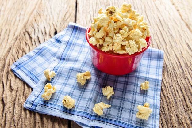 Popcorn dolce casalingo del caramello in una ciotola sul tovagliolo blu del cotone contro fondo di legno