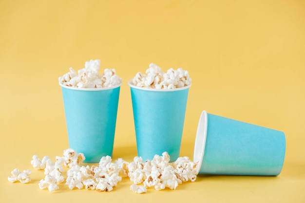 Popcorn in bicchieri di carta blu su sfondo giallo. Copia, spazio vuoto per il testo.