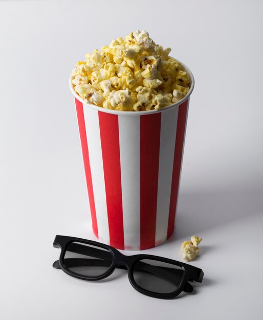 Popcorn in secchio rosso a strisce con i vetri 3d alla tavola bianca.