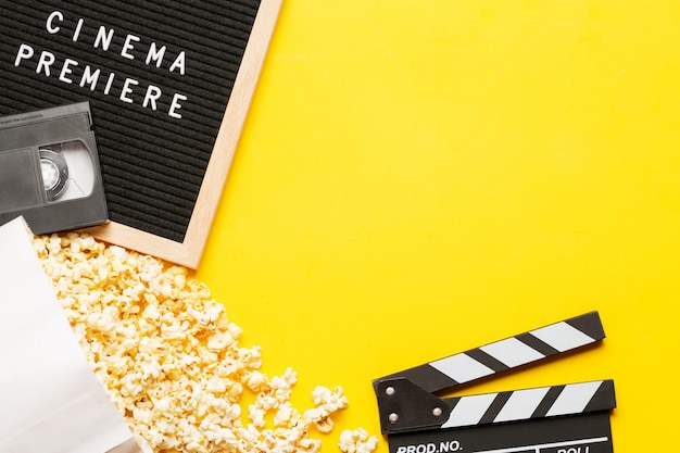 Popcorn in una scatola, batacchio film, videocassetta VHS e bacheca con premiere cinema parole su sfondo giallo.