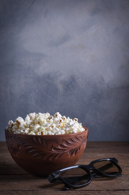 Popcorn salato in una ciotola con occhiali 3D su un tavolo di legno su uno sfondo grigio. Vista frontale