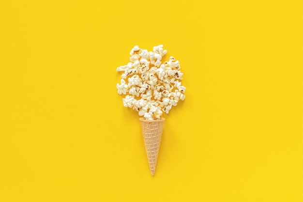 Popcorn sparsi nel cono di cialda gelato su sfondo giallo