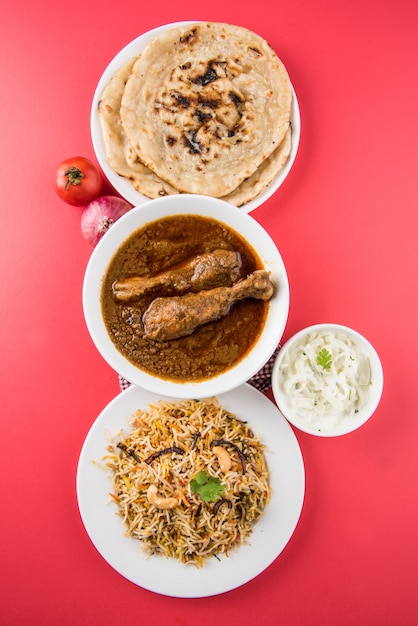 Popolare pollo al curry rossastro o Masala, con un pezzo di gamba prominente, servito in una ciotola con riso Pilau, Chapati o Roti e insalata