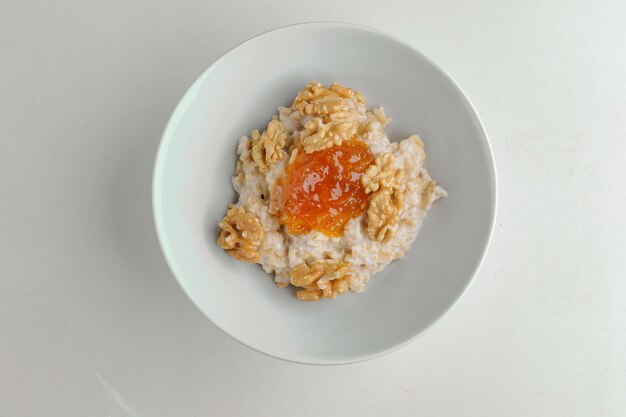 Porridge con marmellata e noci su un piatto bianco su sfondo bianco