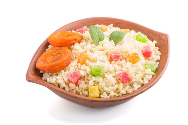 Porridge di bulgur con albicocche secche e frutta candita in una ciotola di argilla isolata. Vista laterale, da vicino. Cucina tradizionale turca.