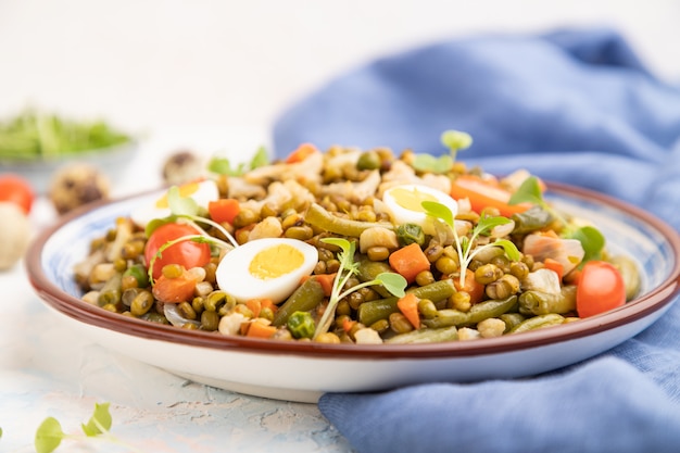 Porridge di fagioli verdi con uova di quaglia, pomodori e germogli di microgreen su uno sfondo di cemento bianco.