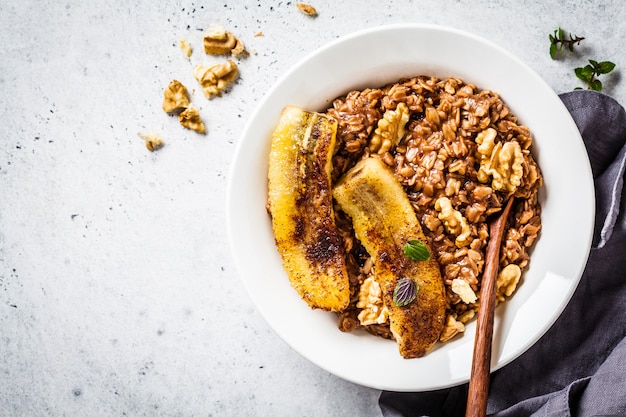 Porridge di farina d'avena al cioccolato con banana fritta e noce in zolla bianca.