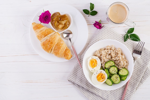 Porridge di farina d'avena colazione con uova sode, cetriolo e croissant, marmellata, caffè. Cibo sano ed equilibrato. Vista dall'alto, posizione piatta