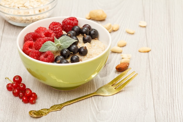 Porridge di farina d'avena con bacche di ribes e lamponi, forchetta, ciotole di vetro con fiocchi d'avena