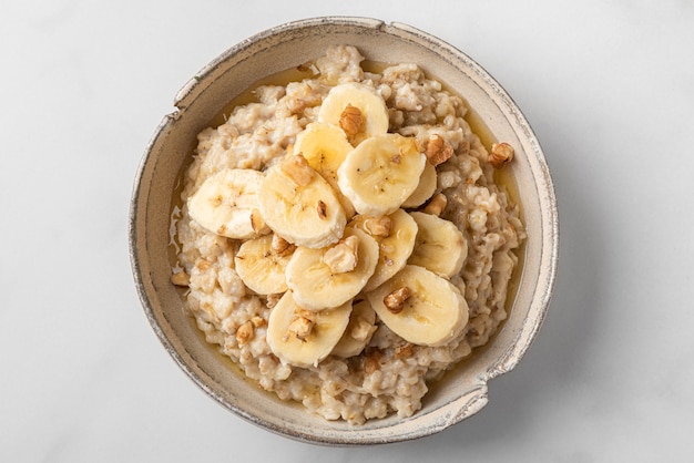 Porridge di farina d'avena con banana, noci e miele in una ciotola su sfondo bianco. Vista dall'alto