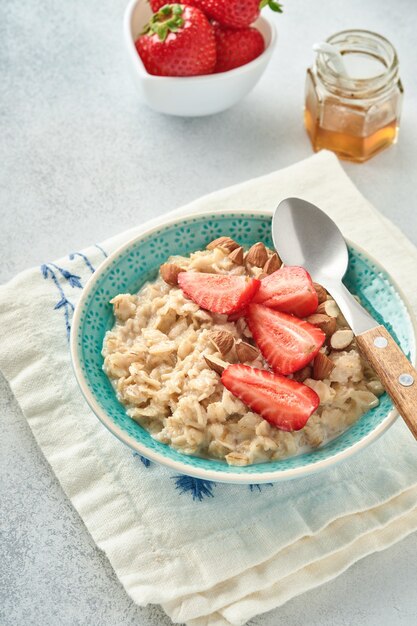 Porridge di farina d'avena con fette di fragola, mandorle noci e miele in una ciotola blu sul tavolo grigio. Mangiare sano, dieta, concetto di cibo vegetariano. Posto per il testo