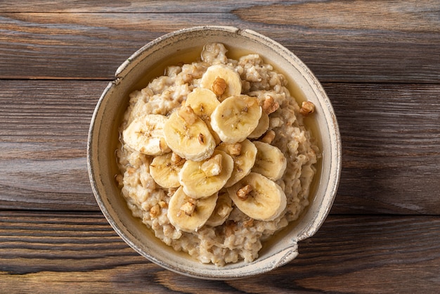 Porridge di farina d'avena in una ciotola con banana, noci e miele su fondo di legno rustico. Vista dall'alto. Colazione salutare