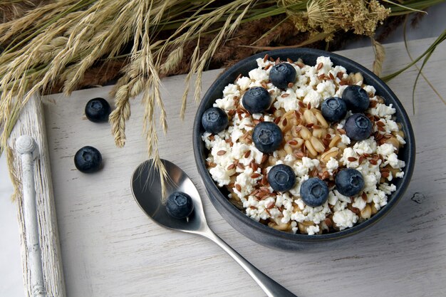 Porridge di farina d'avena integrale con semi di lino e mirtilli su un bianco vintage che serve con un bouquet di erbe secche