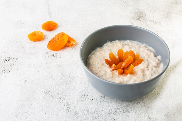 Porridge di farina d'avena o avena di porridge o cereali per la colazione con albicocche secche isolate su fondo di marmo bianco. Cibo fatto in casa. Gustosa colazione Messa a fuoco selettiva. Foto orizzontale.