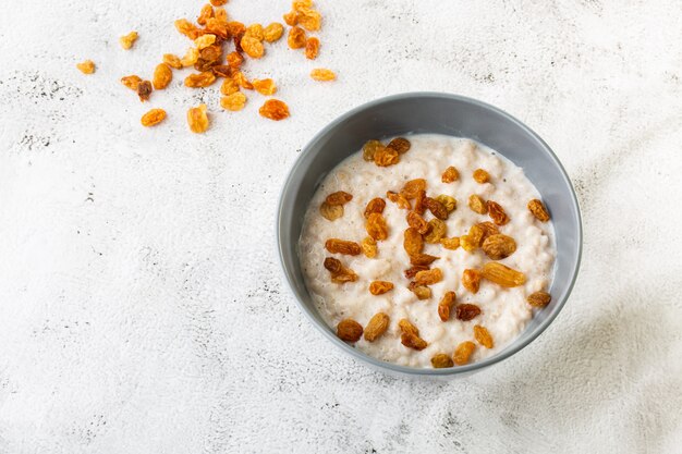 Porridge di farina d'avena o avena di porridge o cereali per la colazione con uvetta isolato su sfondo di marmo bianco. Cibo fatto in casa. Gustosa colazione Messa a fuoco selettiva. Foto orizzontale.