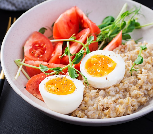 Porridge di farina d'avena per colazione con uovo sodo, pomodorini e microgreens