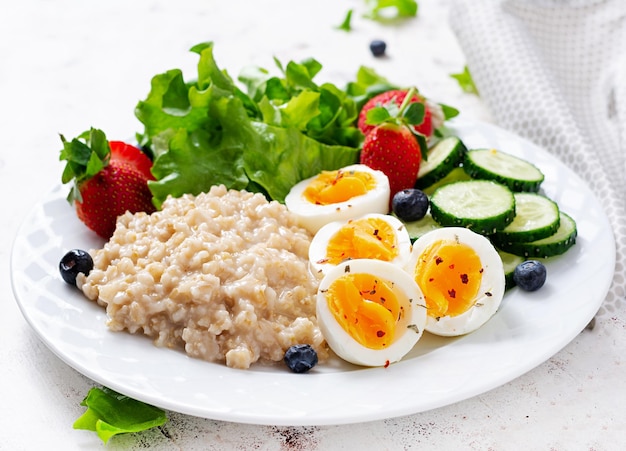 Porridge di farina d'avena per la colazione con uova sode cetriolo e fragola Cibo sano ed equilibrato