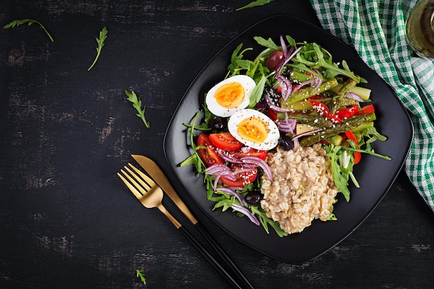 Porridge di farina d'avena per la colazione con uovo sodo pomodorini asparagi e rucola Cibo sano ed equilibrato Vista dall'alto