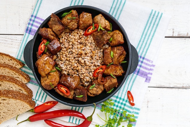 Porridge di grano saraceno con pezzi di maiale fritto, servito su una padella di ghisa