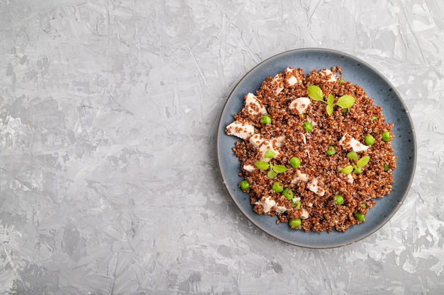 Porridge di quinoa con piselli e pollo sul piatto di ceramica su uno sfondo di cemento grigio.