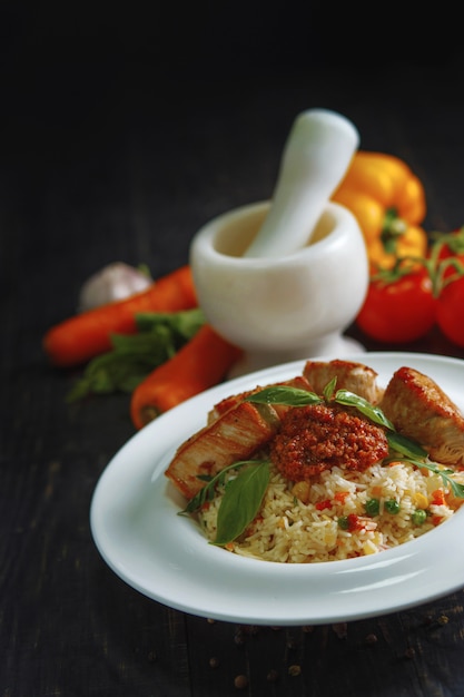 Porridge di riso con verdure e carne su un tavolo di legno nero.