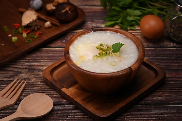 Porridge di riso o congee con uovo sodo morbido affettare lo zenzero e affettare la guarnizione di scalogno sul tavolo di legno