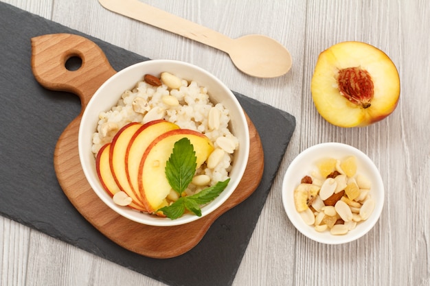 Porridge di sorgo con pezzi di pesca, anacardi e mandorle in ciotole di porcellana, pesca fresca su tavole di legno e pietra. Insalata di sorgo vegana senza glutine con frutta. Vista dall'alto.