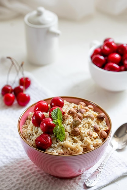 Porridge erculeo con muesli alle nocciole e bacche di ciliegia in un piatto rosa o tavolo bianco