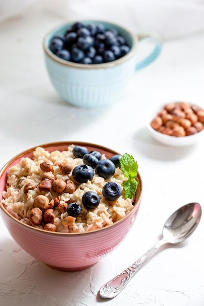 Porridge erculeo con muesli alle nocciole e mirtilli in un piatto rosa o tavolo bianco