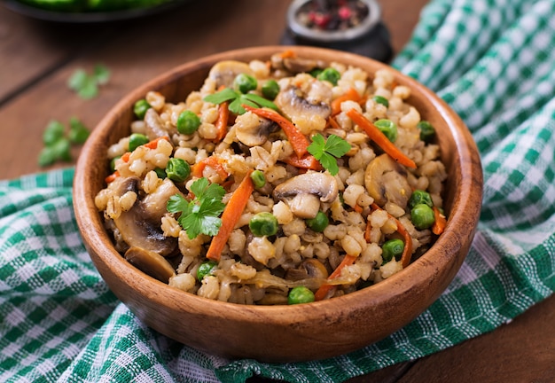 Porridge friabile vegetariano dell'orzo perlato con funghi e piselli in una ciotola di legno