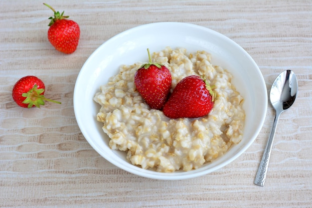 porridge in ciotola bianca con fragola e cucchiaino isolato, macro