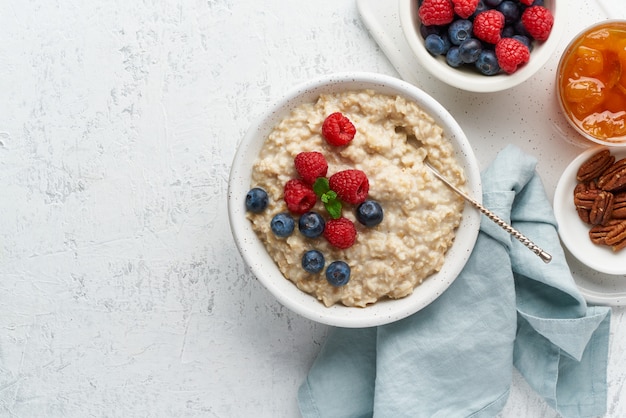 Porridge rustico di farina d'avena con mirtilli, lamponi, marmellata e noci in una ciotola bianca, un trattino dieta