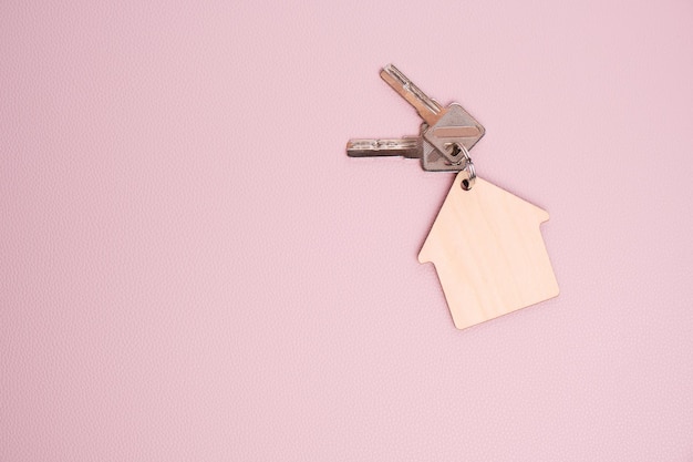 Portachiavi in forma di casa con chiavi sfondo rosa Concetto di acquisto casa appartamento o affitto