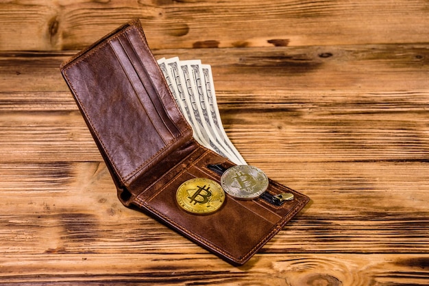 Portafoglio in pelle marrone bitcoin e banconote da cento dollari sullo sfondo di legno