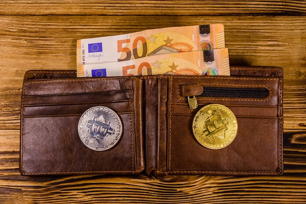 Portafoglio in pelle marrone con cinquanta banconote in euro e bitcoin sullo sfondo di legno. Vista dall'alto